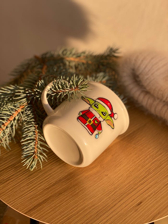 Festive mug with Santa design next to pine branches, perfect for cozy holiday vibe.
