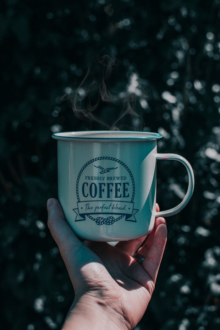 Hand holding a steaming coffee mug outdoors with an artistic vintage feel.