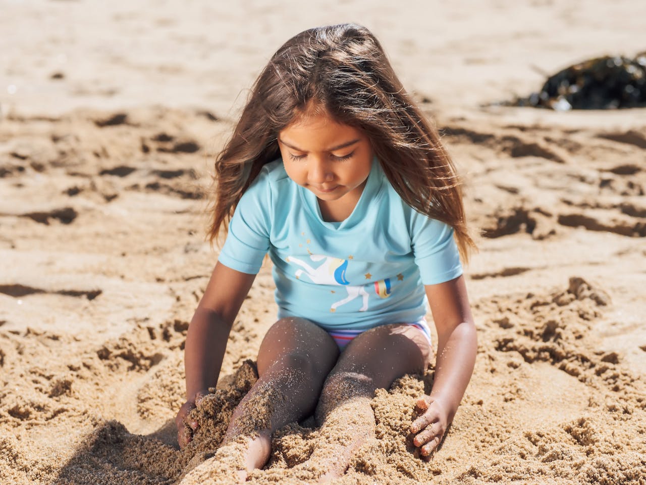 Young girl plays with sand on a sunny beach, enjoying a carefree summer day.